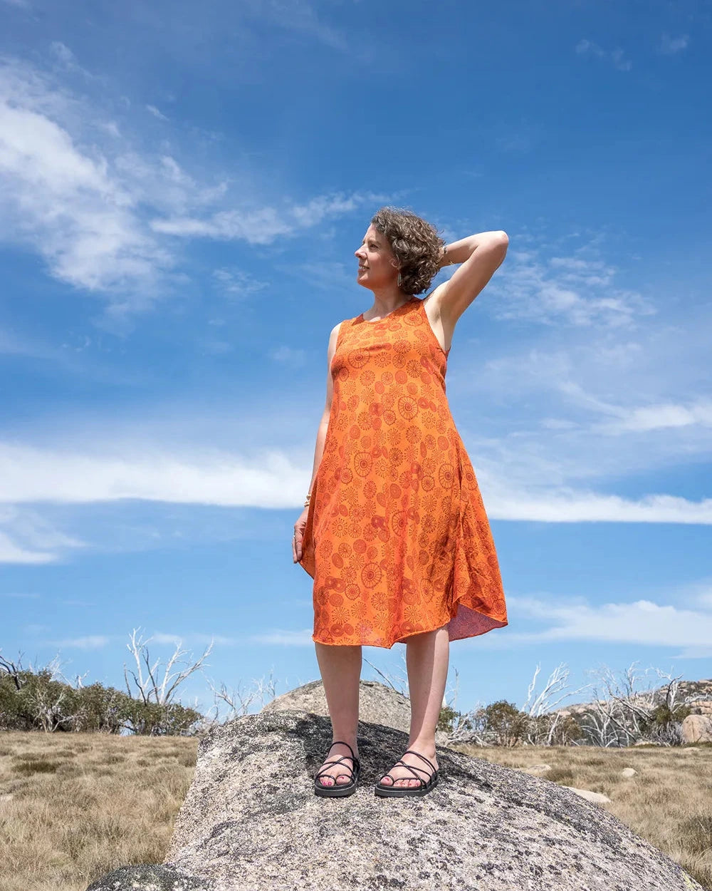 Woman in an orange dress standing on a rock with a blue sky and clouds in the background