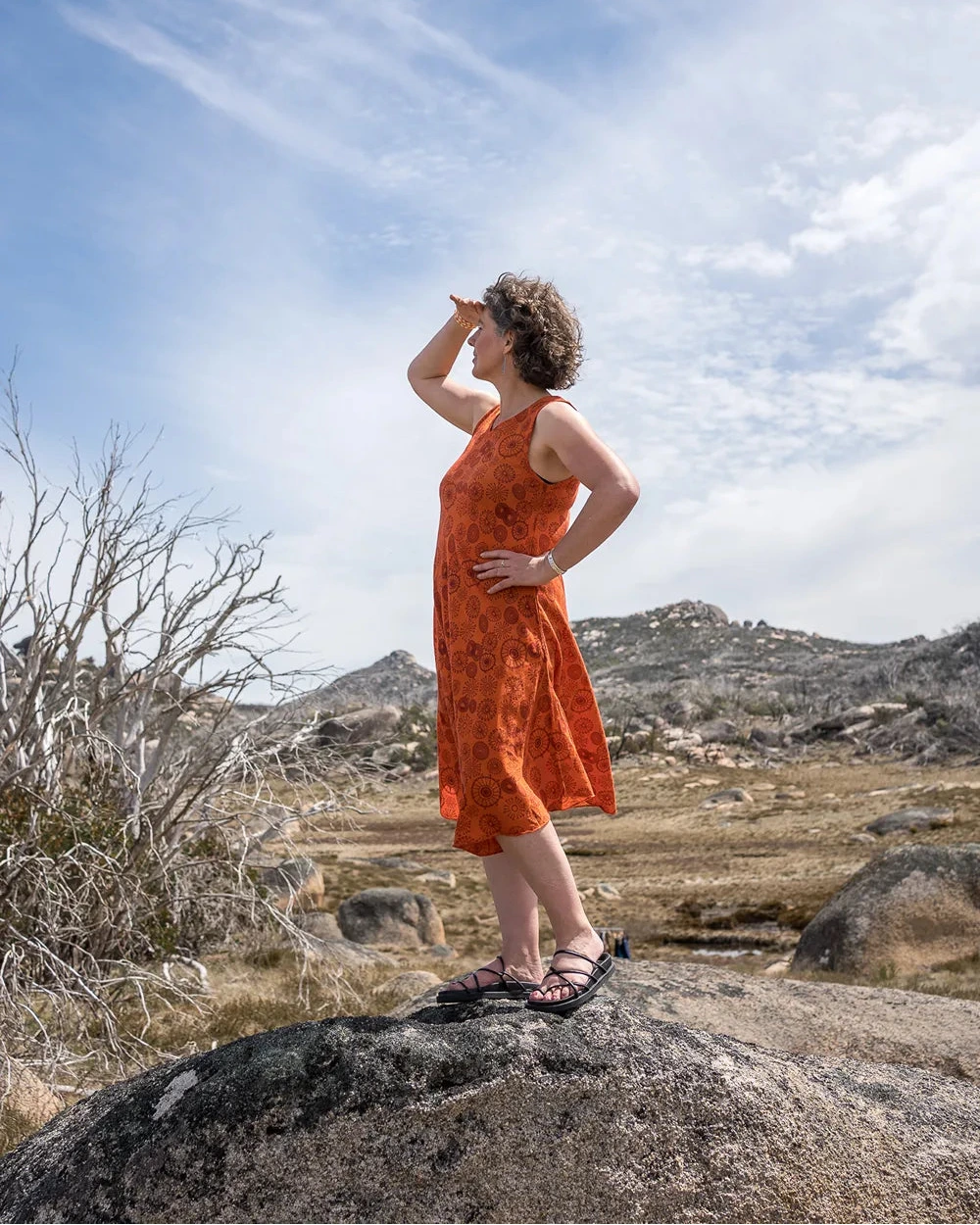 Woman in an orange dress standing on a rock in a desert landscape with mountains in the background.