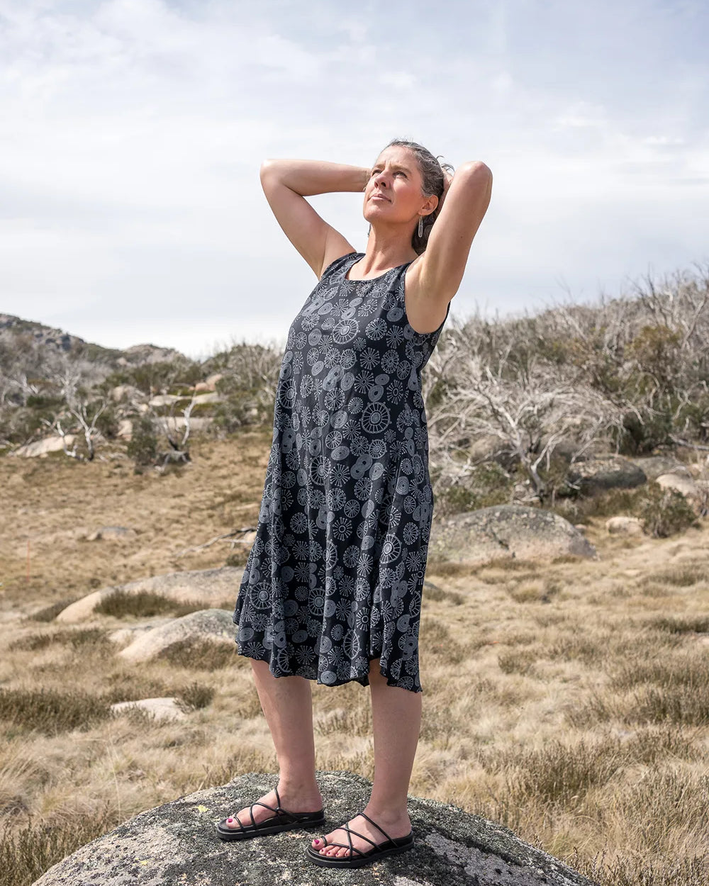 Woman in a sleeveless dress standing on a rock in a natural landscape
