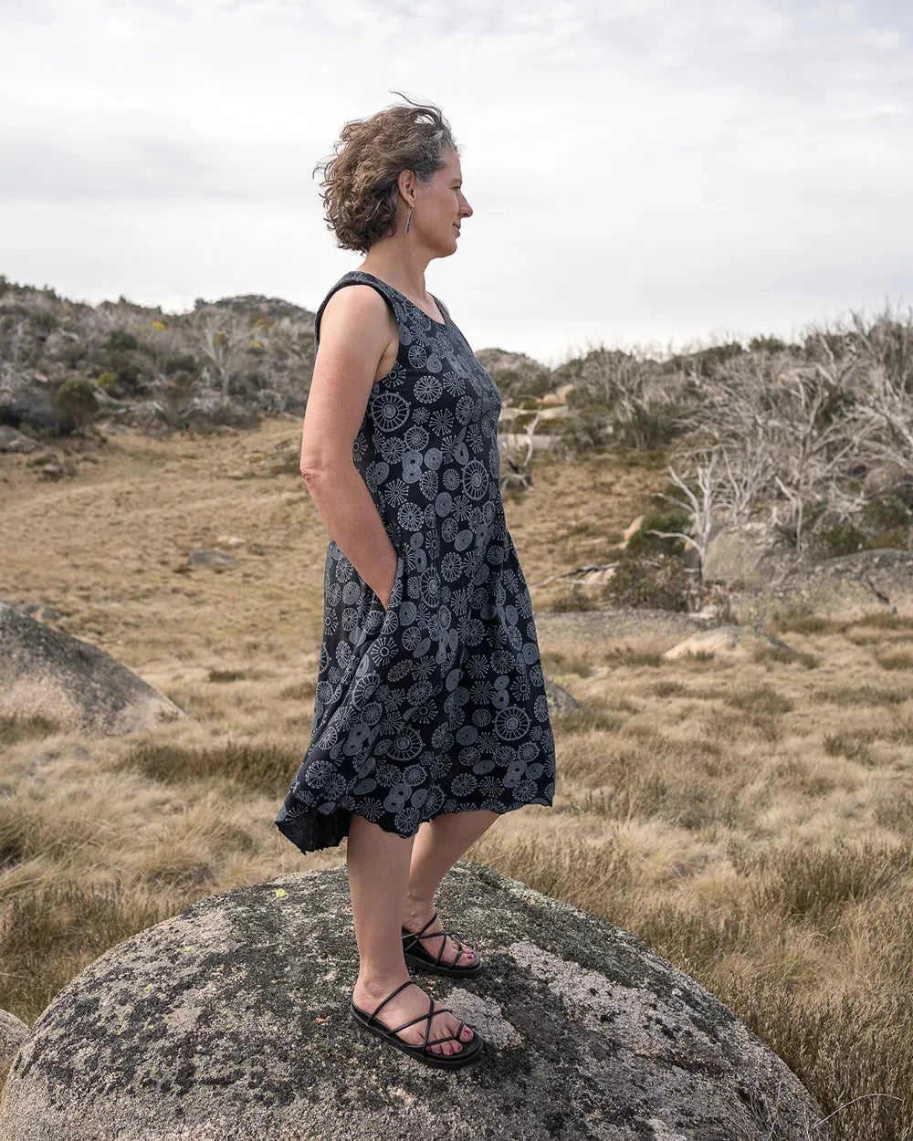 Woman in a black patterned dress standing on a rock in a desert landscape