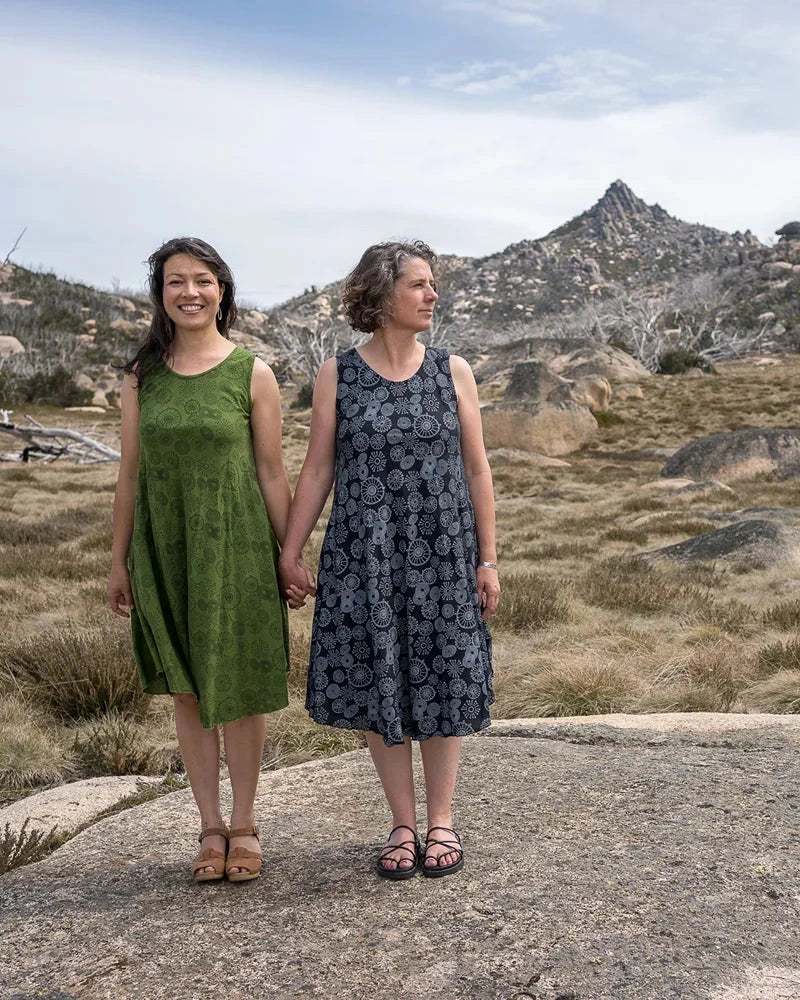 Two women standing on a rocky outcrop with a mountainous landscape in the background.