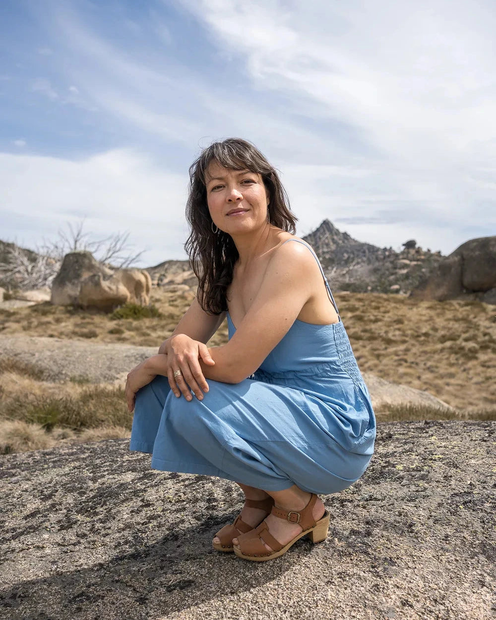 Woman in a blue jumpsuit squatting on a rocky landscape with a clear sky.