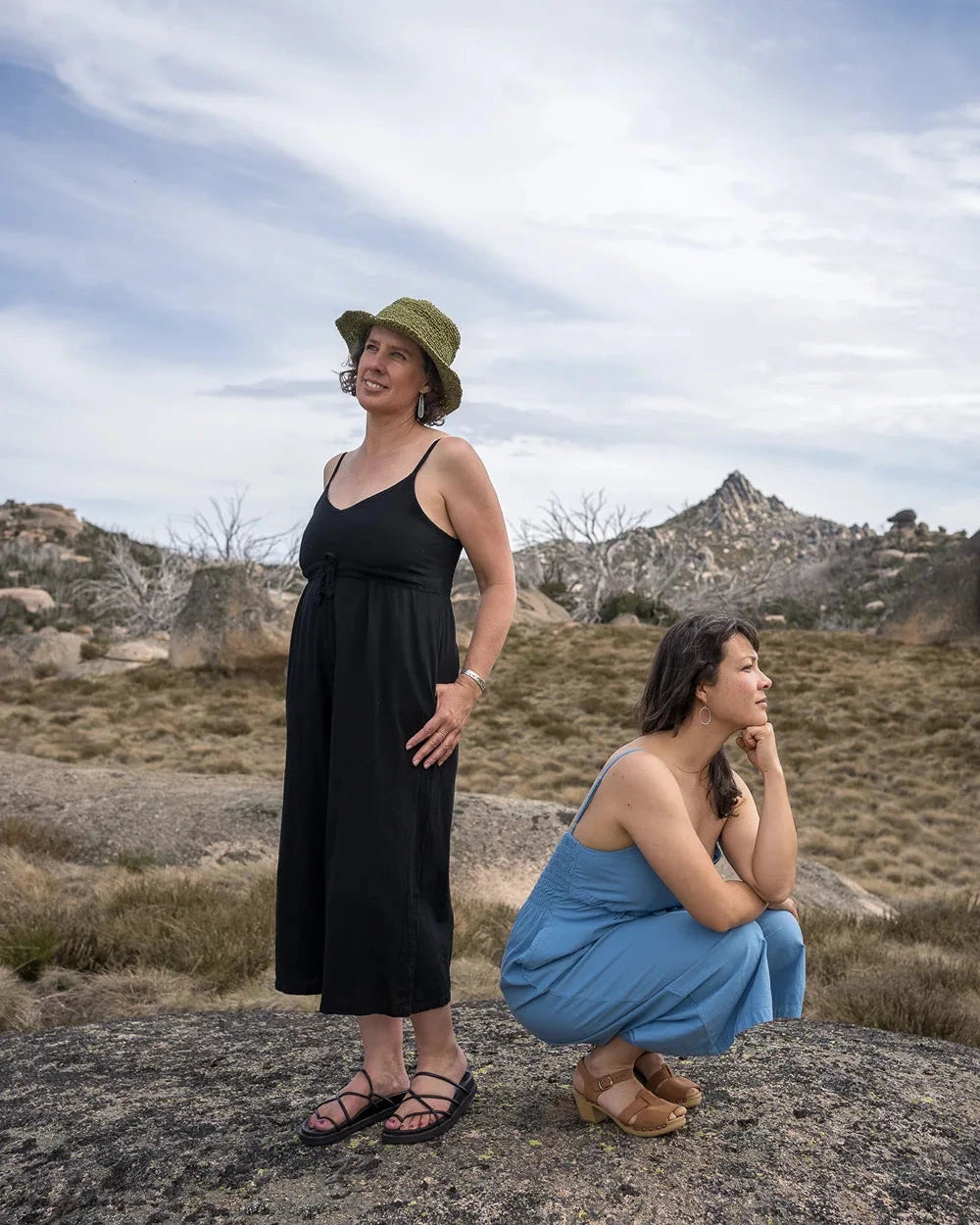 Two women standing on a rocky outcrop with a scenic landscape in the background