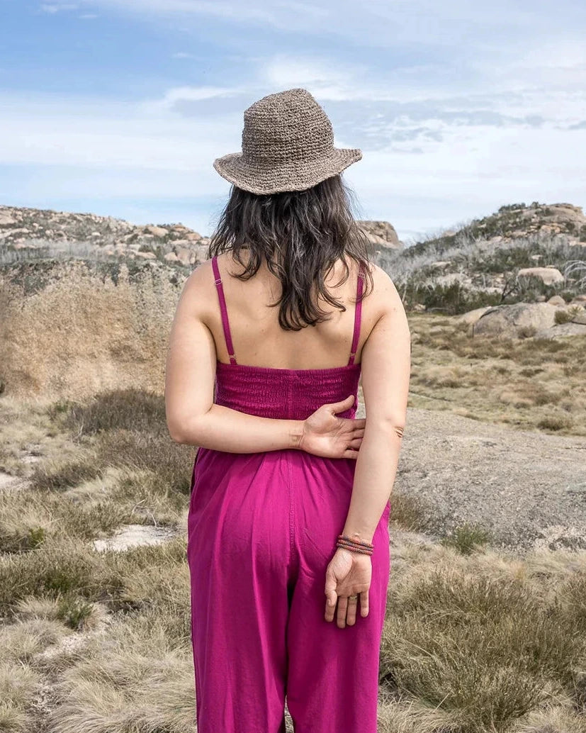 Woman in a pink dress and straw hat standing in a desert landscape