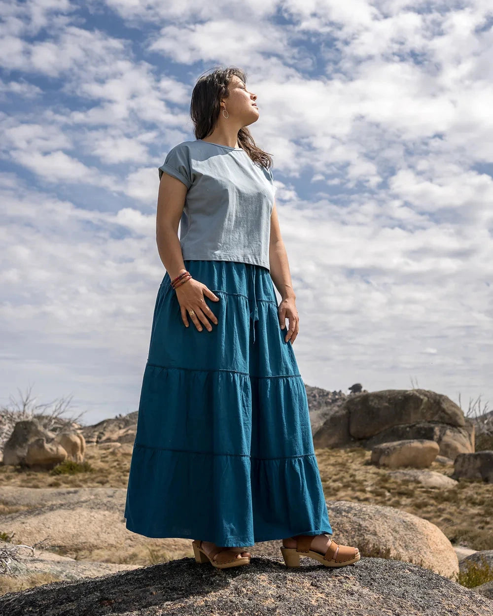 Woman in a blue skirt standing on a rocky landscape with a cloudy sky.