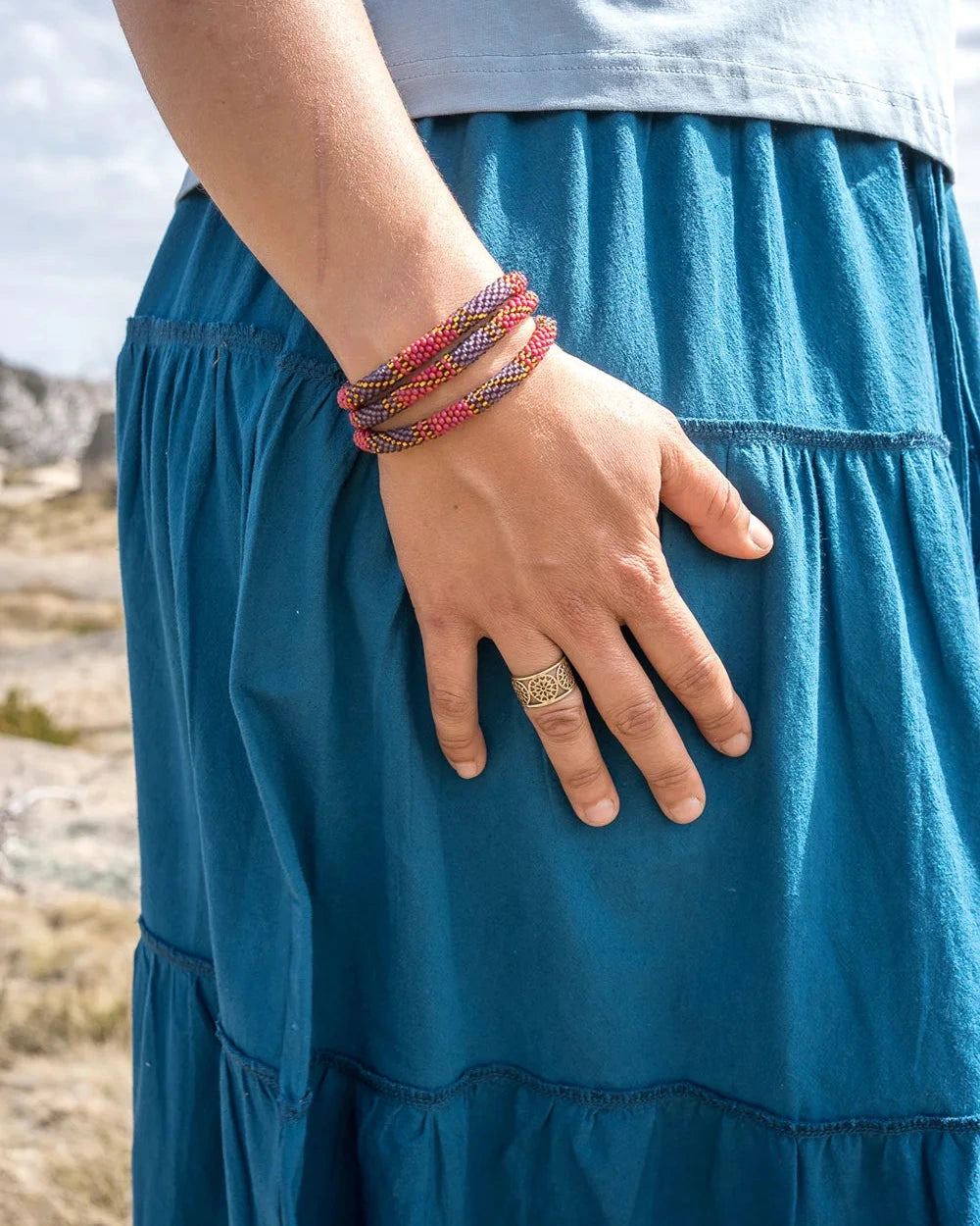 Person wearing a blue skirt with a colorful bracelet and ring, outdoors.