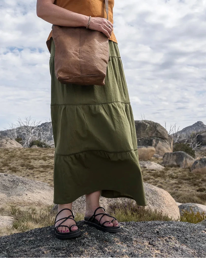 Woman standing outdoors with a brown bag against a cloudy sky