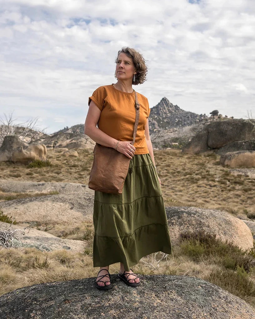 Woman in a green skirt standing on a rocky landscape with mountains in the background