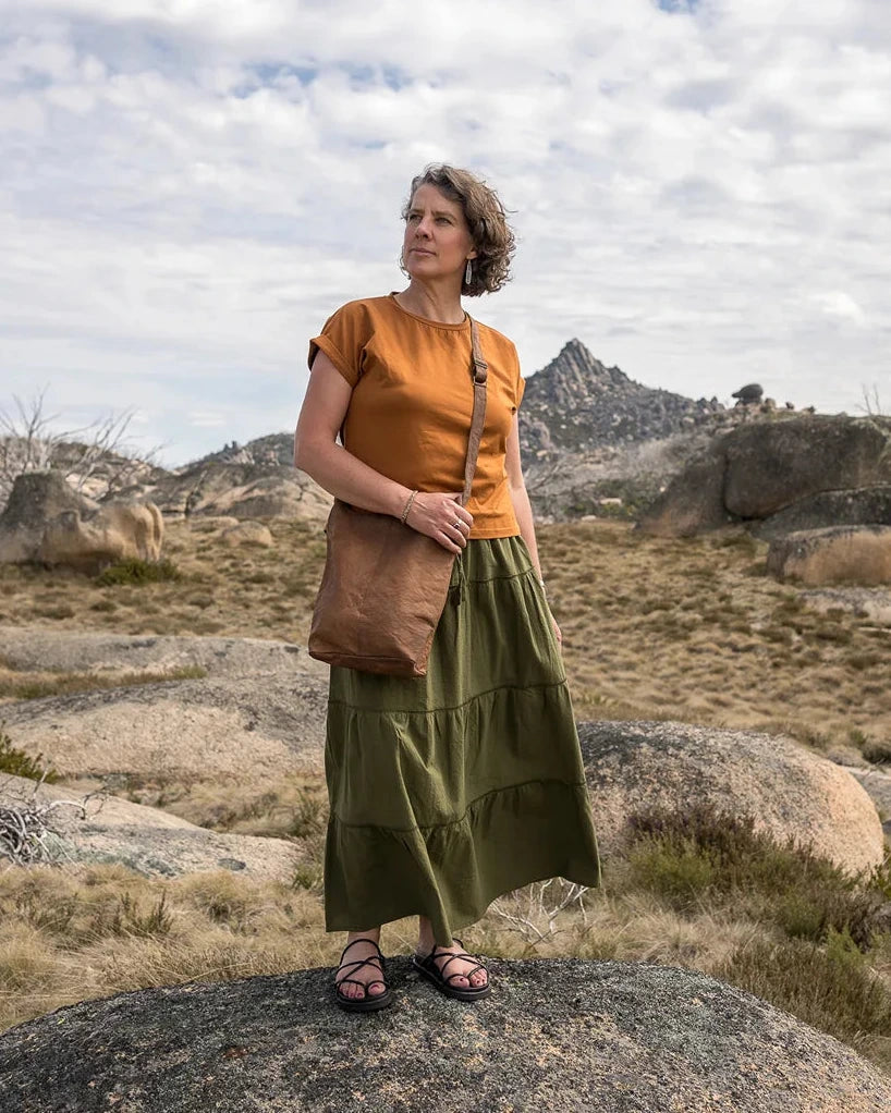 Woman in a green skirt standing on a rocky landscape with mountains in the background
