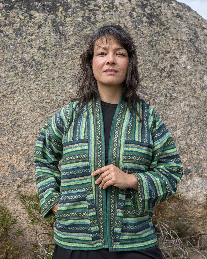 Person wearing a green patterned jacket standing in front of large rocks