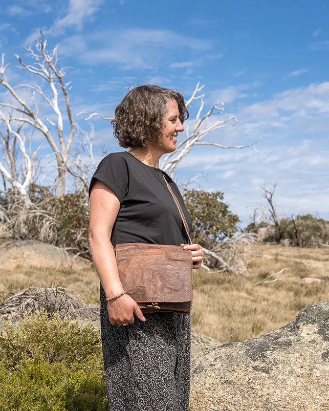 Person standing on a rocky outcrop with a blue sky and trees in the background