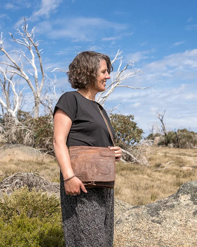 Person standing on a rocky outcrop with a blue sky and trees in the background
