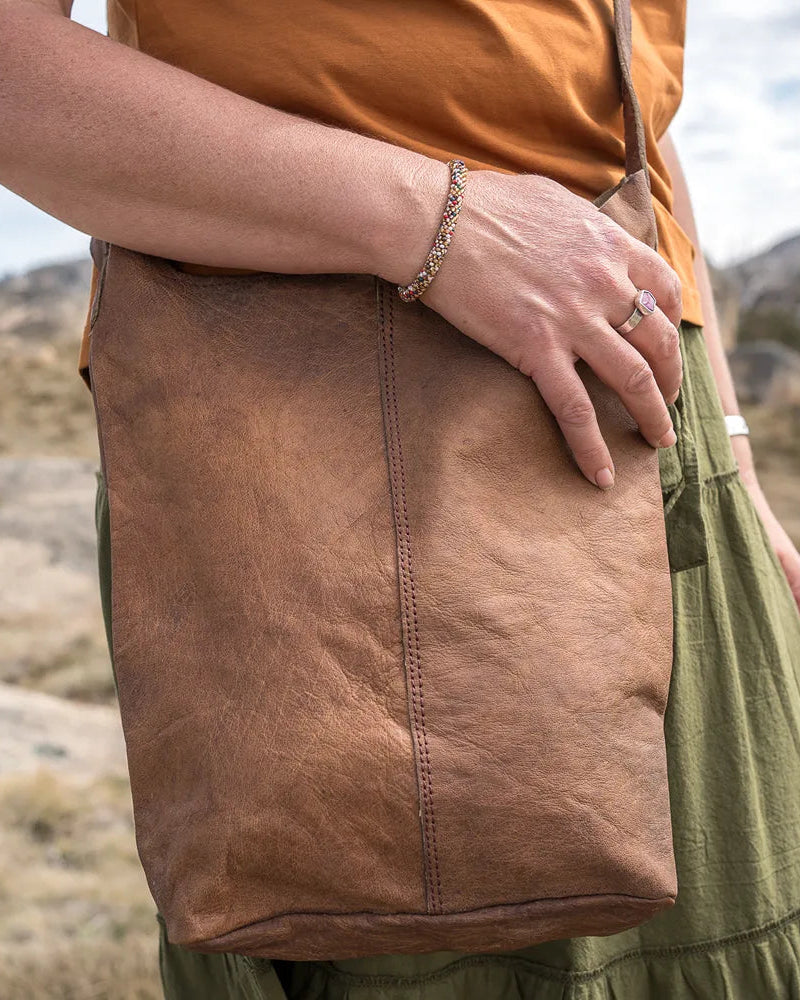 Person holding a brown leather bag in a desert landscape