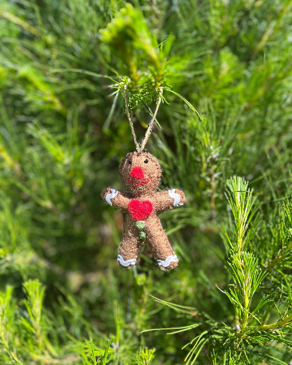 Handmade ornament shaped like a figure with red hearts hanging on a green tree.