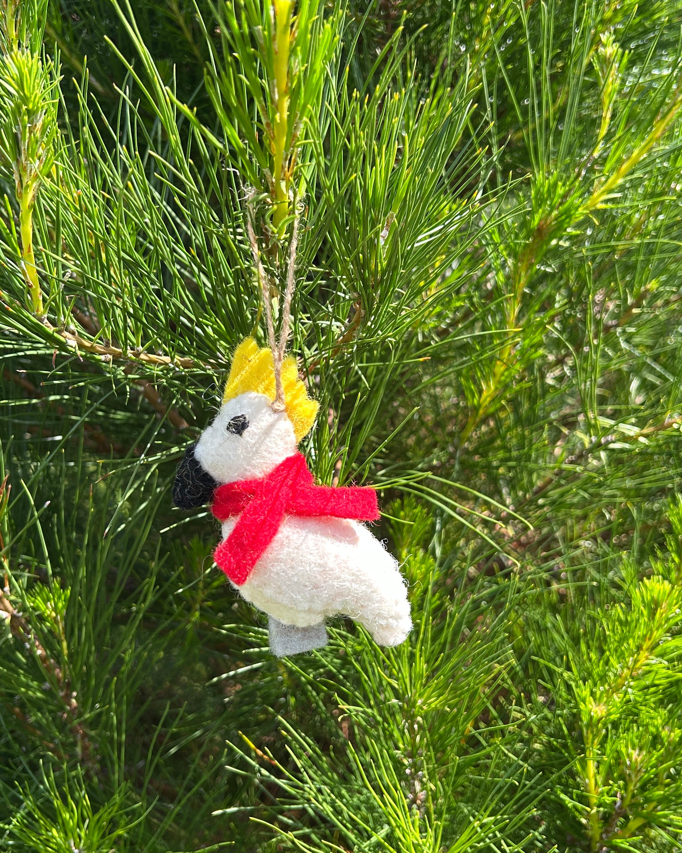 Decorative cockatoo ornament with a red scarf and yellow top hat hanging from a tree.