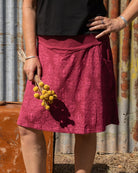 Woman standing with a suitcase and flowers against a rustic corrugated metal wall.