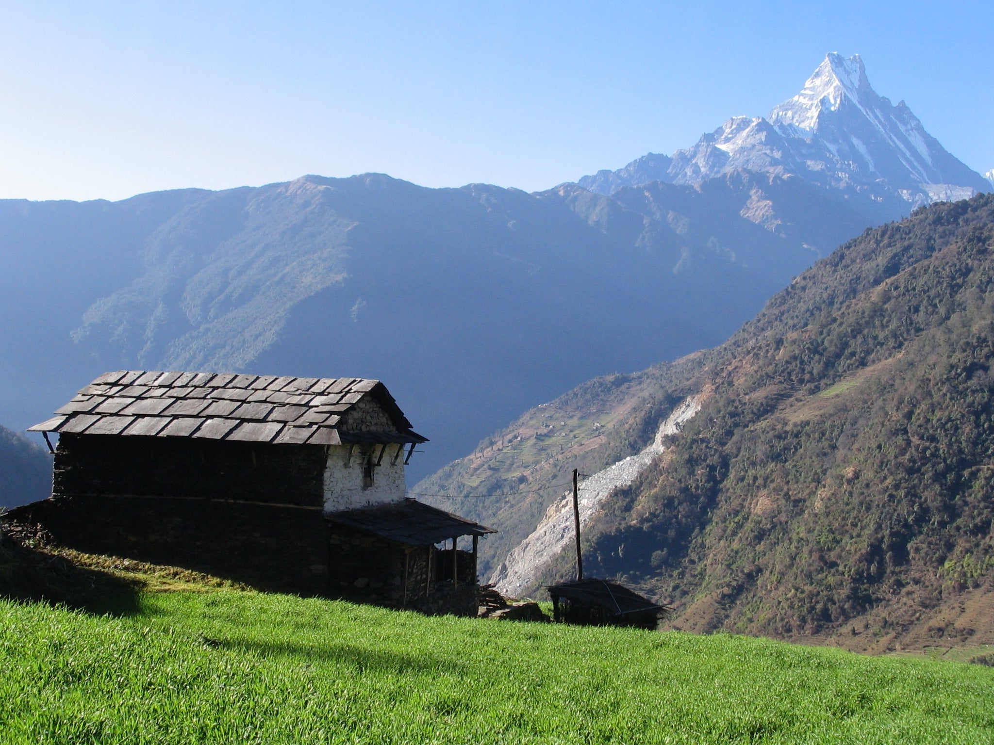 Traditional nepalese wooden house on a grassy hill with snow-capped mountains in the background