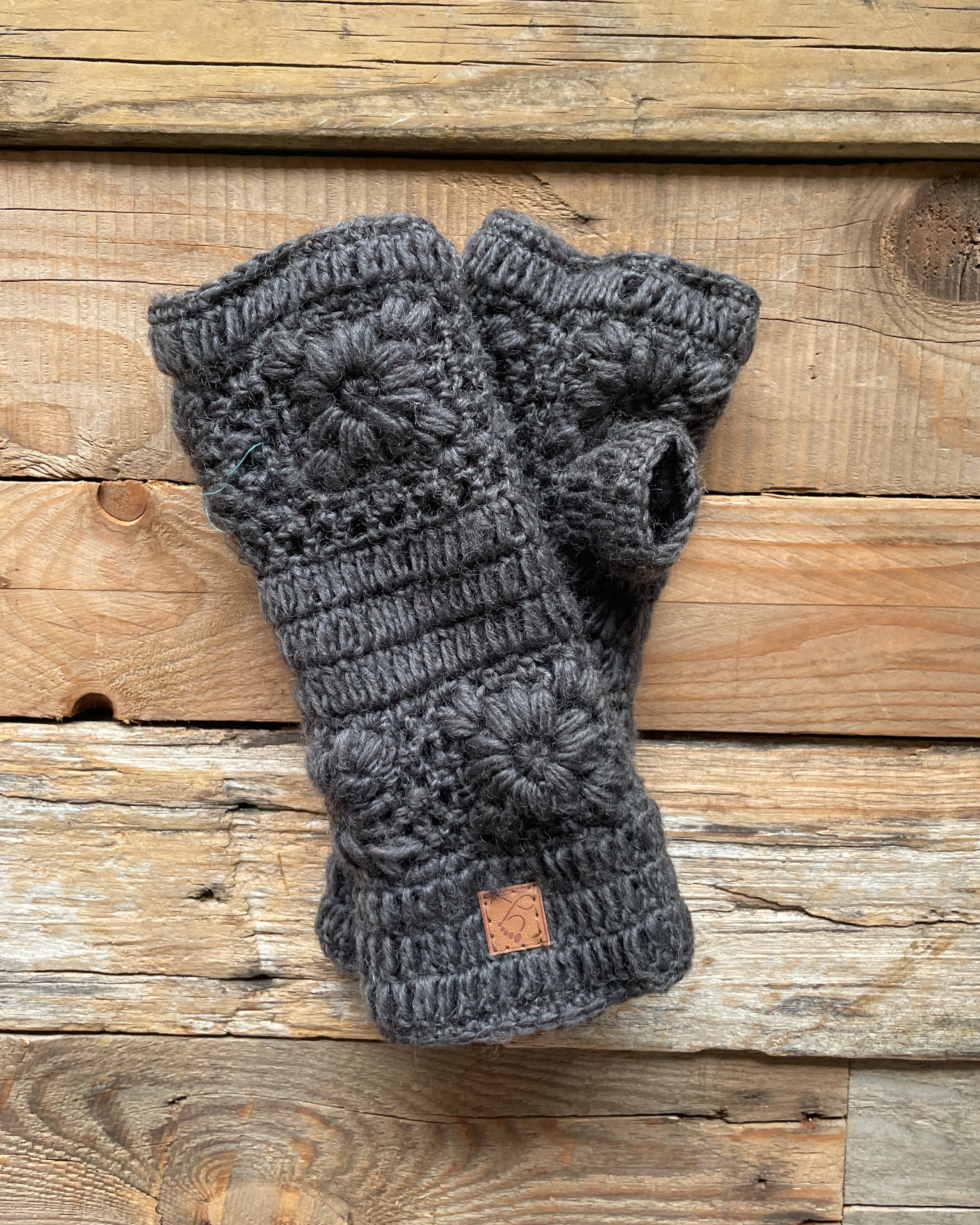 Pair of gray crochet fingerless gloves on a wooden surface