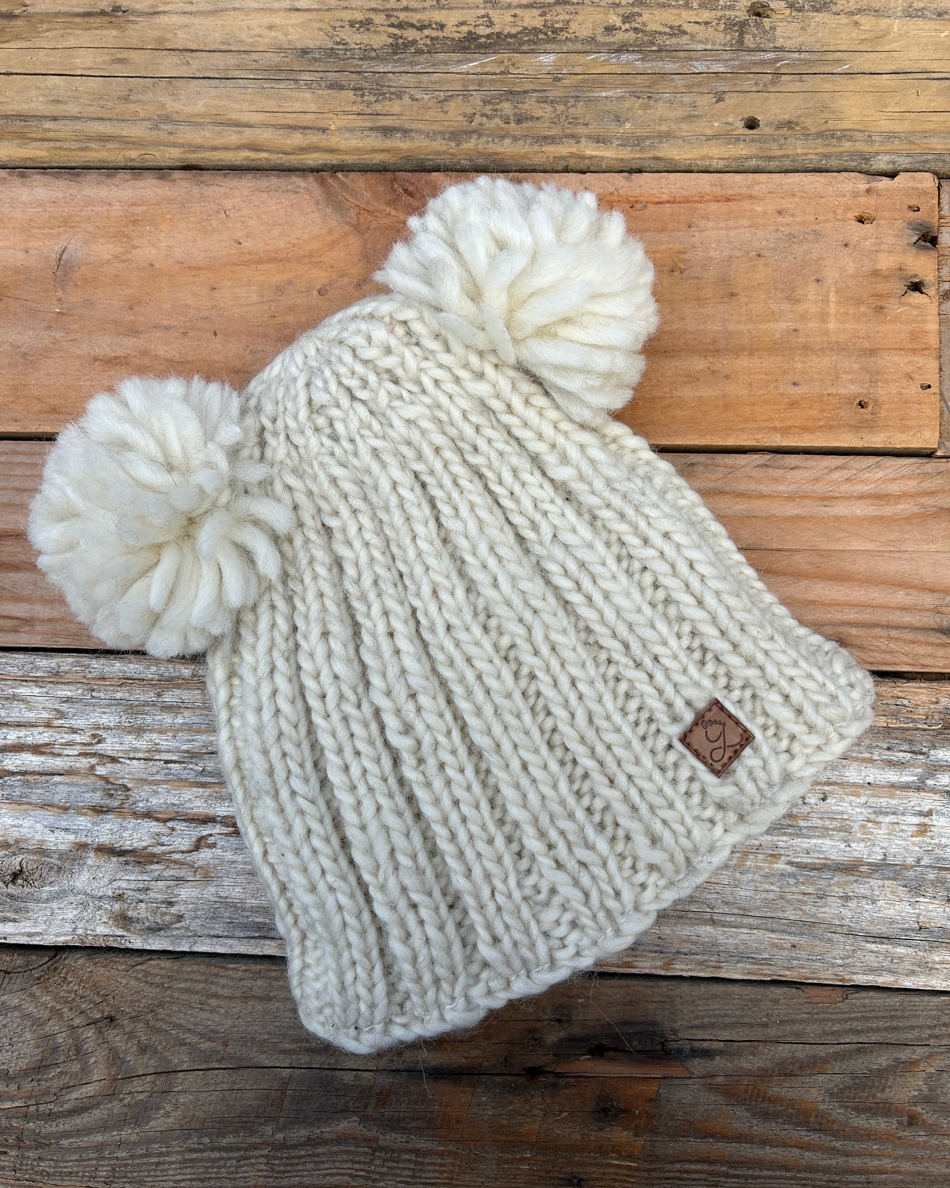 Knitted beanie with pom-poms on a wooden surface