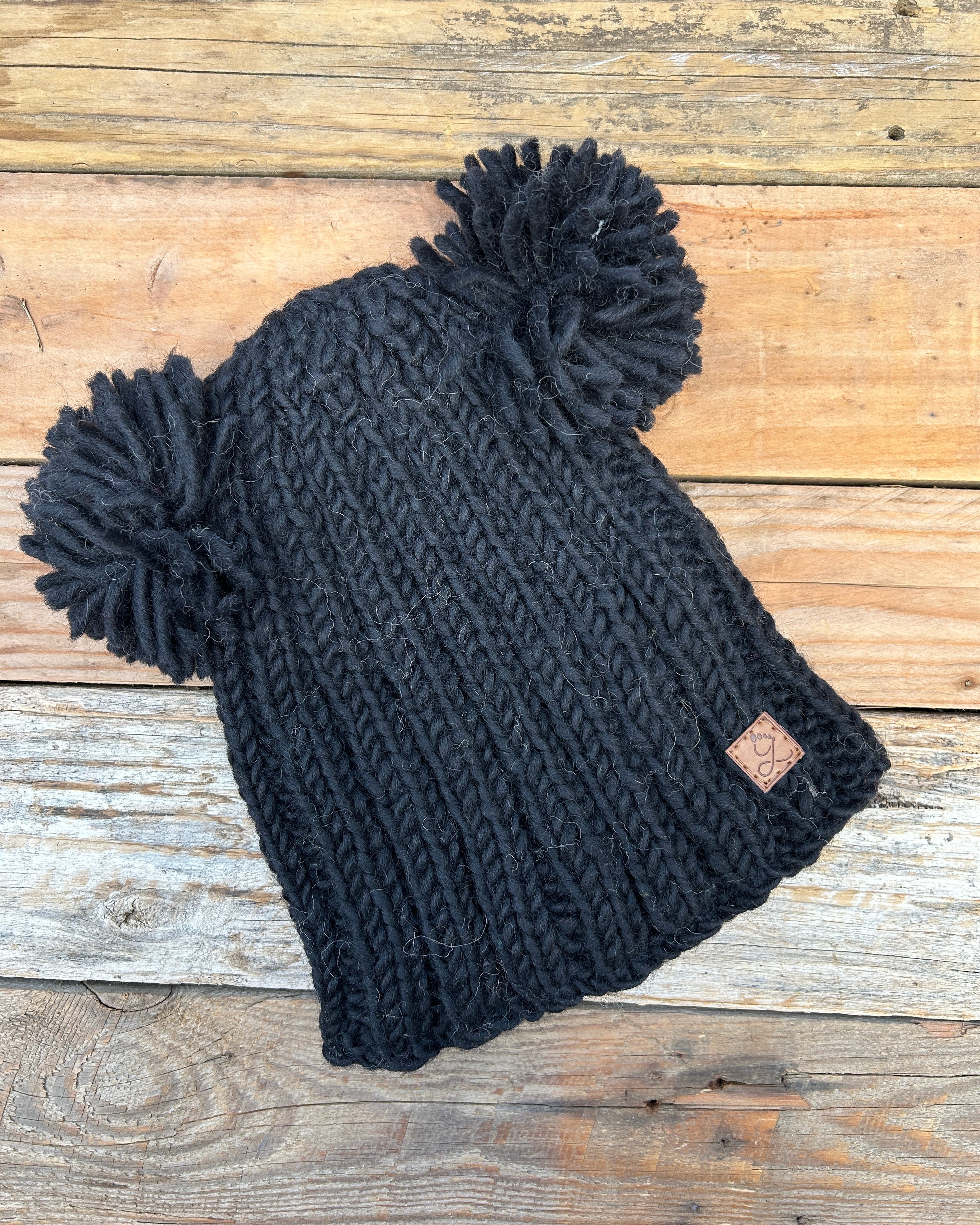 Black knit beanie with pom-poms on a wooden surface
