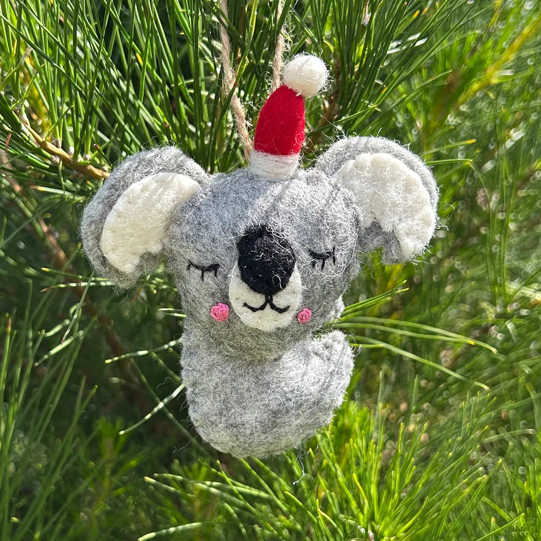Plush koala toy with a red hat hanging on green foliage