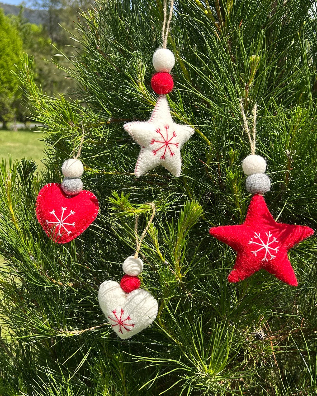 Felt Christmas ornaments shaped like stars and hearts hanging on a tree.