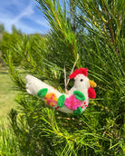 Decorative chicken ornament with colorful feathers hanging in a tree.