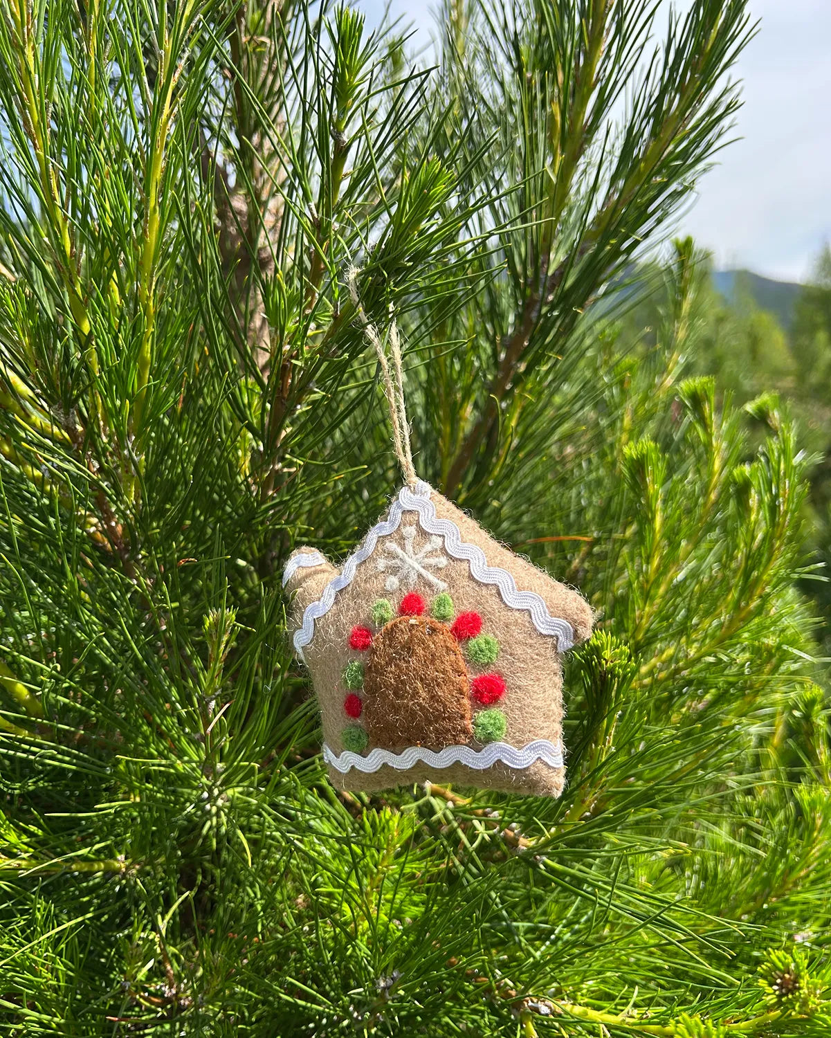 Decorative gingerbread house ornament hanging on a pine tree