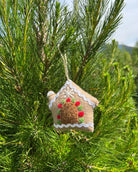 Decorative gingerbread house ornament hanging on a pine tree