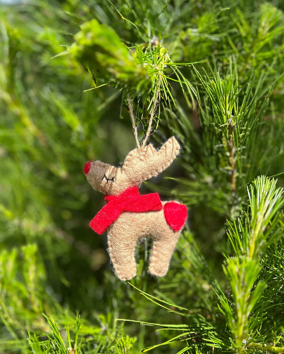 Small reindeer ornament with a red scarf hanging on a Christmas tree.