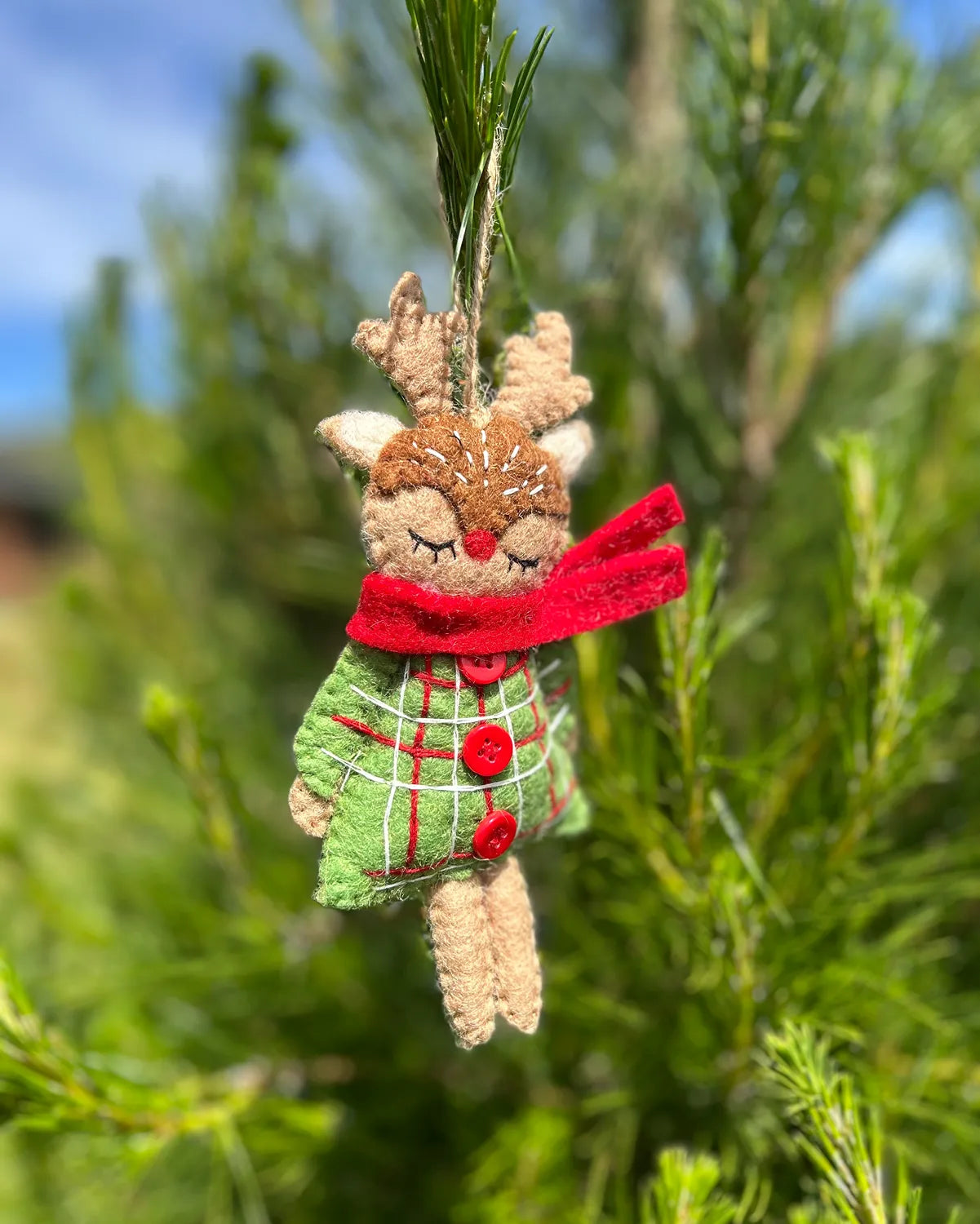 Decorative reindeer ornament with a red scarf and green dress hanging on a tree.