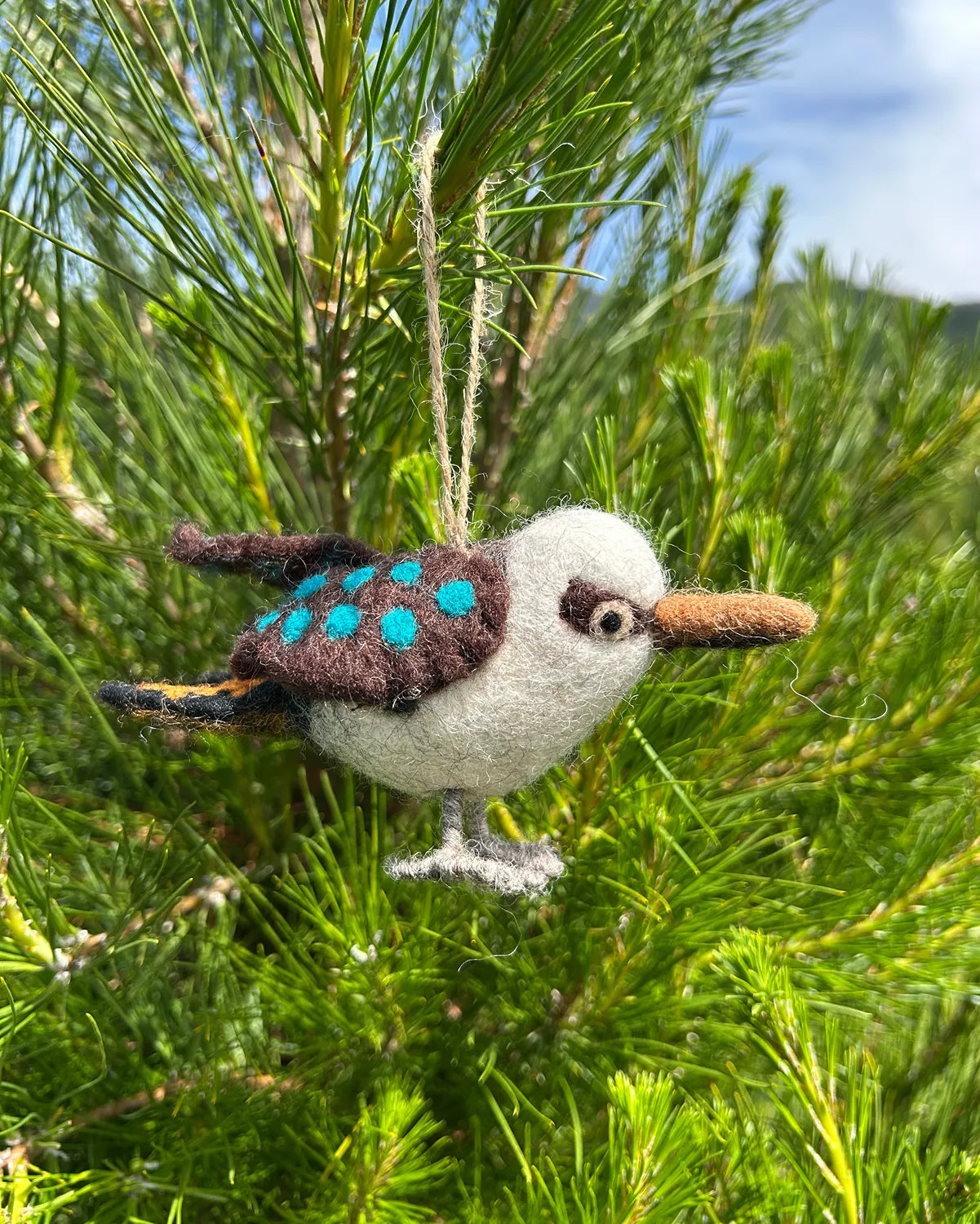 Felted bird ornament hanging from a pine tree
