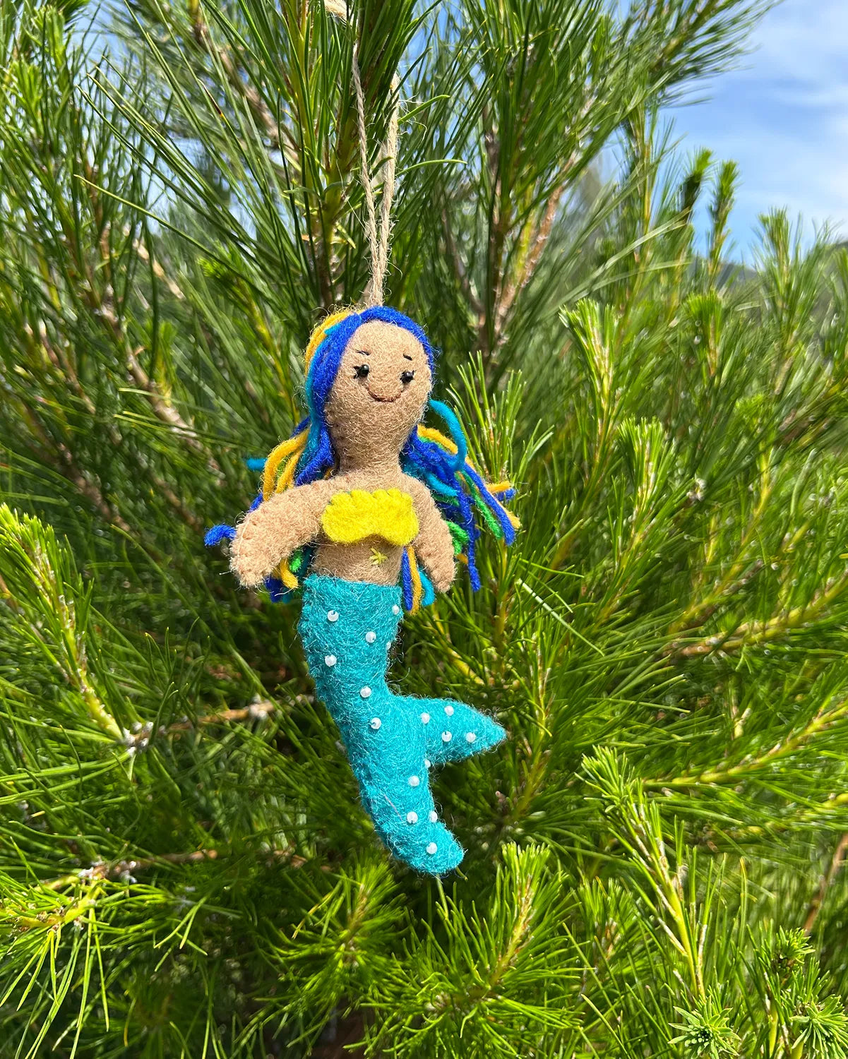 Mermaid ornament with blue hair and tail hanging from a pine tree