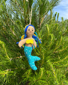 Mermaid ornament with blue hair and tail hanging from a pine tree