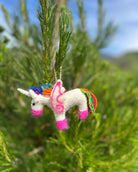 Colorful unicorn ornament hanging on a tree branch with a blurred natural background