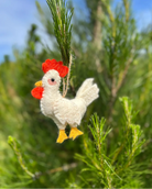 Felt chicken ornament hanging on a tree branch with a blurred natural background