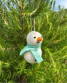 Small snowman ornament with a green scarf hanging in a pine tree.