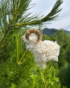 White sheep ornament hanging on a pine branch with a mountainous background