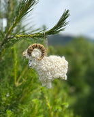 White sheep ornament with brown horns hanging from a tree branch