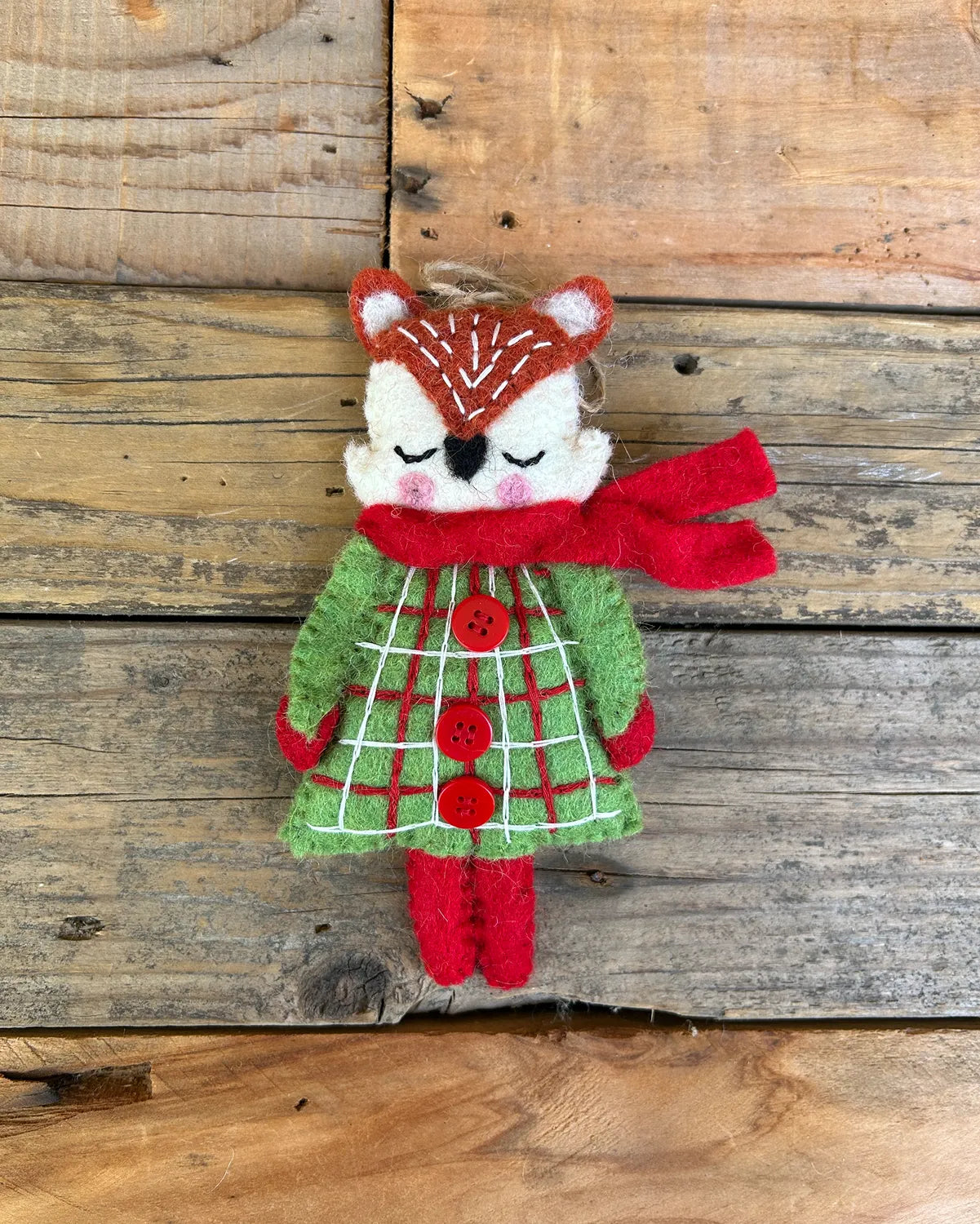 Stuffed animal fox wearing a green dress with red buttons and a red scarf on a wooden background