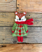 Stuffed animal fox wearing a green dress with red buttons and a red scarf on a wooden background