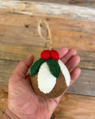 Felted Christmas pudding ornament held in a hand against a wooden background