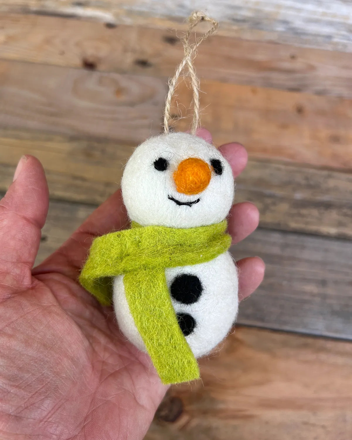 Felted snowman ornament with a green scarf hanging from a tree.