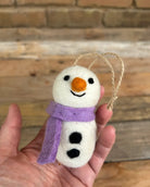 Small snowman ornament with a purple scarf held in a hand against a wooden background