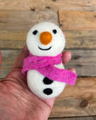 Small snowman ornament with a pink scarf held in a hand against a wooden background