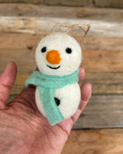 Small snowman ornament with a blue scarf held in a hand against a wooden background