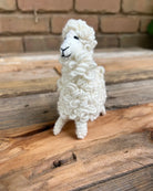 White knitted llama toy on wooden steps with a brick wall background