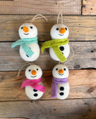 Four felt snowman ornaments with colorful scarves on a wooden background