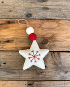 Decorative star ornament with red snowflake design and white pom-pom on a wooden surface