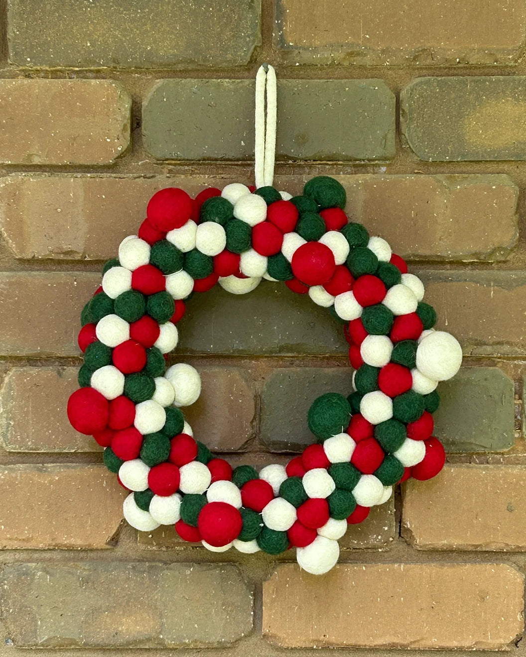 Colorful felt ball wreath hanging on a brick wall